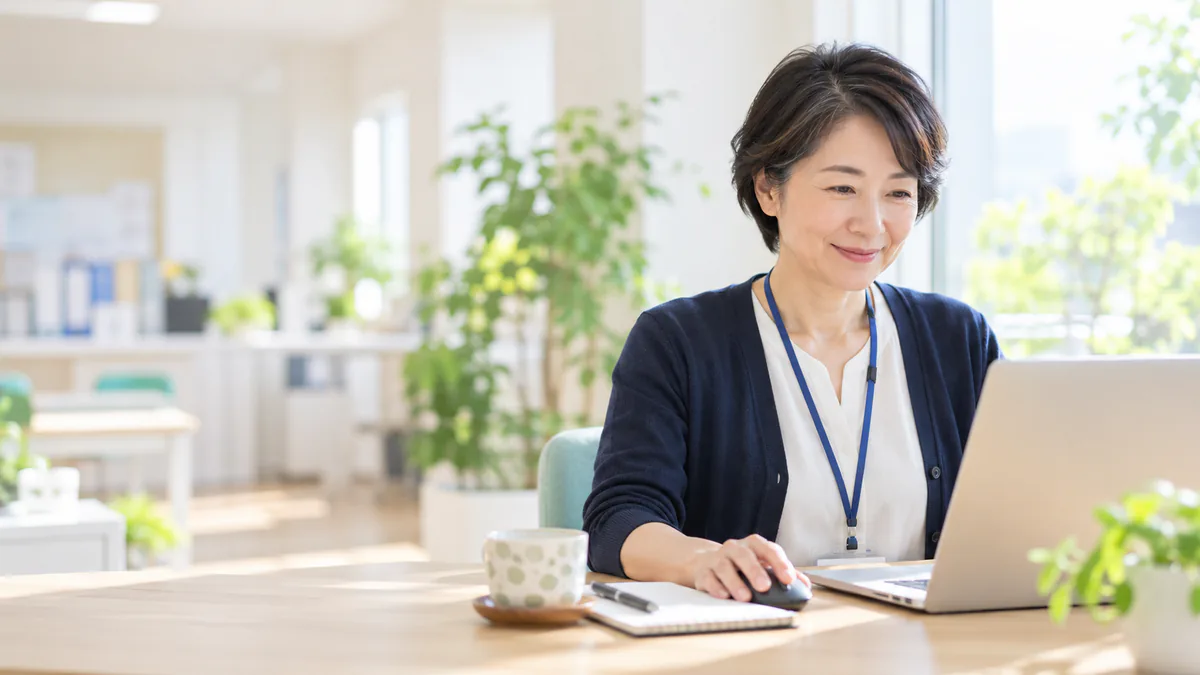 ノートパソコンで記録を確認している、職員証を下げた保健師